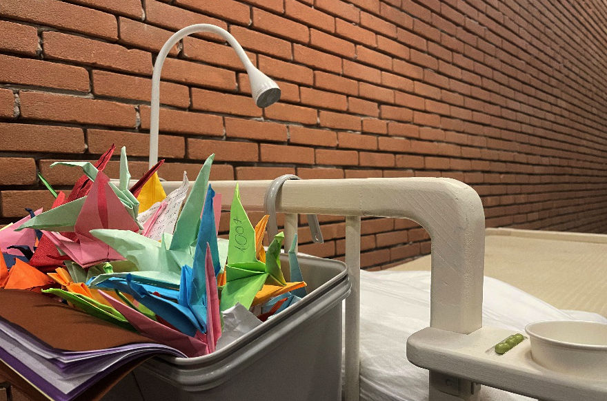 Il bordo di un letto con un cesto con origami colorati di fianco ad un muro di mattoni